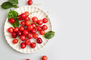 Plate with sweet cherries and leaves on white background