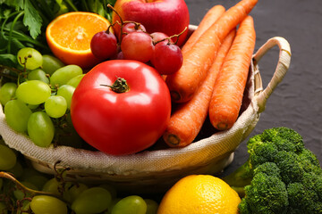Wicker basket with different fresh fruits and vegetables on black background, closeup