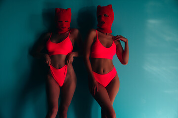 Dark light. Two beautiful sexy women in red underwear. Models wearing bandit balaclava mask. Hot...