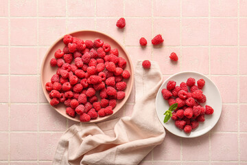 Plates with fresh raspberries on pink tile background