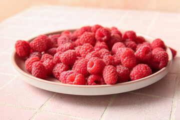 Plate with fresh raspberries on pink tile background