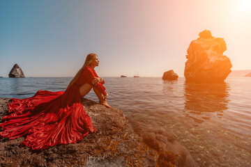 woman sea red dress. Beautiful sensual woman in a flying red dress and long hair, sitting on a rock...
