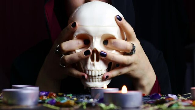 Witch hands holding a scary skull for a black magic ritual on a magical altar. Sorcerer rite of witchcraft and occultism. Halloween occult, esoteric and divination concept.