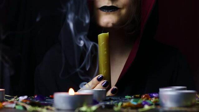 Witch hands performing a magic ritual blowing off a candle on a magical altar. Sorcerer rite of witchcraft and occultism. Halloween occult, esoteric and divination concept.