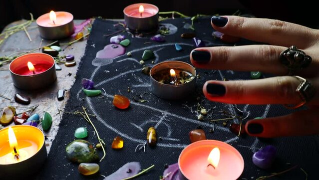 Witch hands performing a black magic ritual with the help of magical altar, candles, crystals and herbs. Sorcerer rite of witchcraft and occultism. Halloween occult, esoteric and divination concept.
