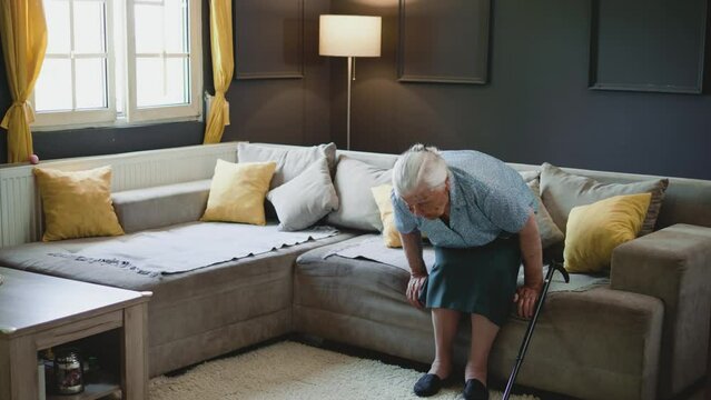 Senior old 80s woman standing up from the sofa with a walking cane stick to walk at home, Elderly suffering from back pain ache holding the handle of cane, retirement medical healthcare
