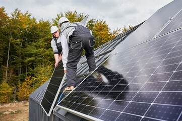 Men roofers installing solar panel system on roof of house. Technicians in helmets lifting up...