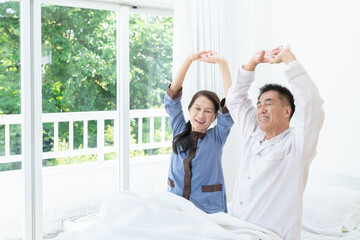 Obraz na płótnie Canvas 朝ベッドでストレッチする笑顔の高齢者夫婦