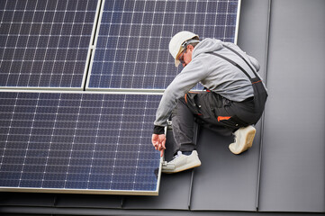 Man technician mounting photovoltaic solar panels on roof of house. Engineer in helmet installing...