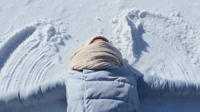 Young woman making a snow angel playing in snow on sunny winter day