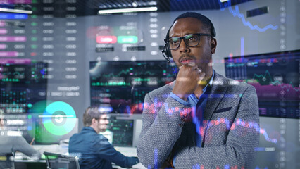 African American investment specialist analyzes real-time stocks in office. 3D graphics of cryptocurrency charts on glass wall. Futuristic VFX animation. Employees work on computers on background.
