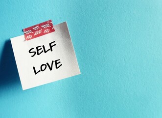Paper note stick on blue copy space background with handwritten text SELF LOVE, refers to self worth, being confidence with self-esteem - giving yourself respect, dignity and understanding