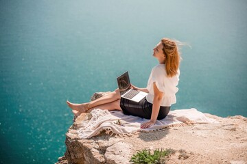 Freelance woman working on a laptop by the sea, typing away on the keyboard while enjoying the...