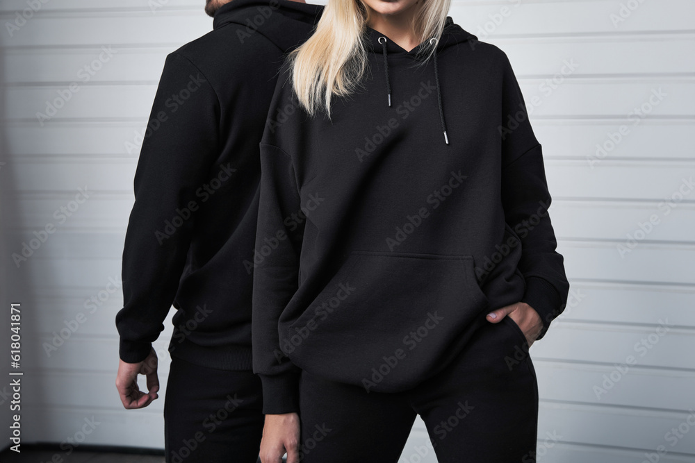 Sticker Stylish Hoodie Mockup. Fashionable Autumn Streetwear for Young Couples. Woman and man wear black hoodies without a logo. No logo basic sportswear. Long sleeve sweatshirt mockup