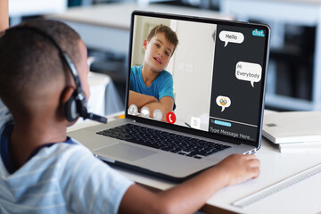 Diverse schoolboys with headphones having laptop video call with chat