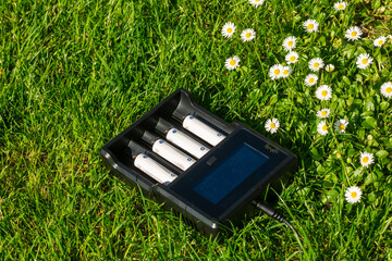 Black AA battery charger with rechargeable alkaline batteries  on the grass. The battery is...