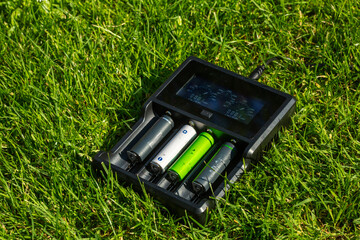 Black AA battery charger with rechargeable alkaline batteries  on the grass. The battery is charging.