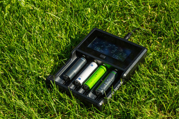 Black AA battery charger with rechargeable alkaline batteries  on the grass. The battery is...