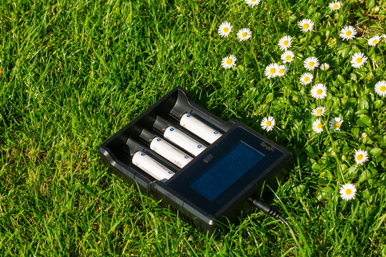 Black AA battery charger with rechargeable alkaline batteries  on the grass. The battery is charging.