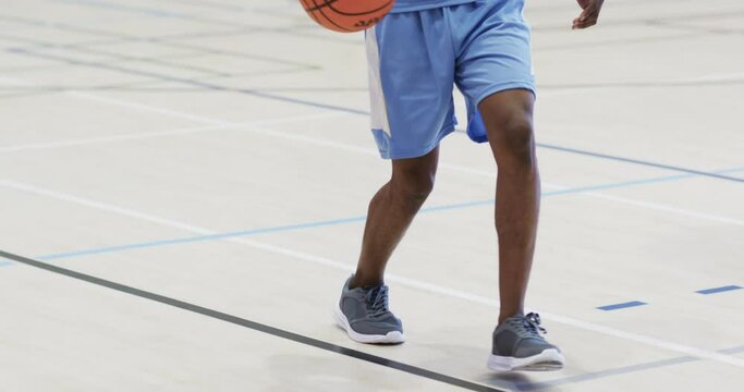 Midsection of african american male basketball player bouncing ball at indoor court, slow motion