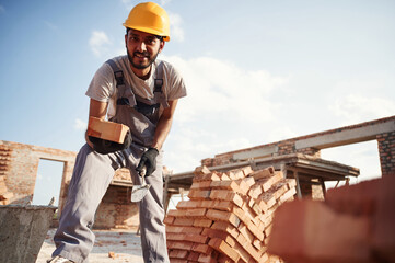 View from below. Brick in hand. Handsome Indian man is on the construction site