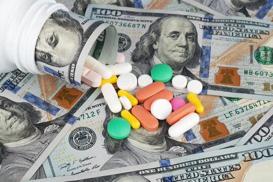 Medicine pills spilling out of pill bottle on dollar banknotes background. The concept of expensive medicine.