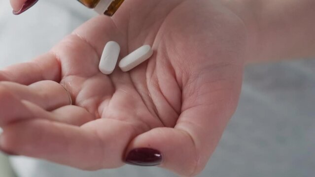 Woman Taking Painkiller White Pills Or Antibiotic On Female Hand Pouring Tablets From Meds Bottle