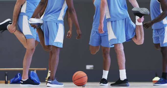 Low section of diverse male basketball players stretching legs at training session, slow motion