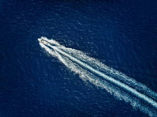 High aerial view of a motor speeboat traveling over blue ocean and leaving a trail of fom and...