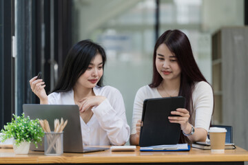 Two young Asian businesswomen talk, consult, discuss working with new startup project idea presentation, and analyze plan marketing and investment in the office.