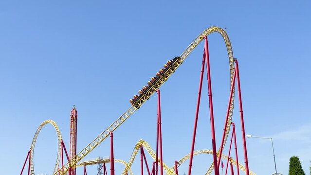 Amusement trolley cart makes uphill downhill and sharp turns upside down circular loops, yellow and red roller coaster in the amusement park, other attractions in the distance free fall.