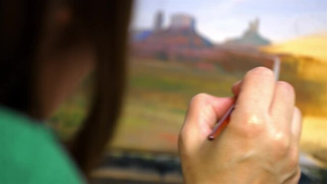 Delicate artist oil painting a scenic desert scape, hand and brush in focus
