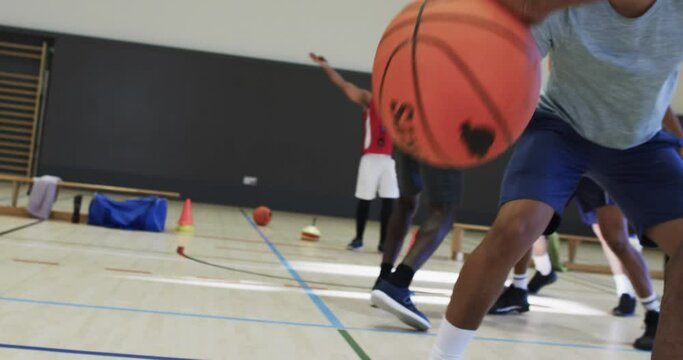 Diverse male basketball players passing ball and blocking during game at indoor court, slow motion
