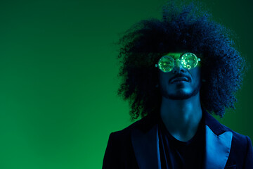 Fashion portrait of a man with curly hair on a green background with sunglasses, multinational, colored pink light, trendy, modern concept.