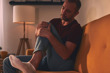 Man with knee pain sitting on a sofa at home.