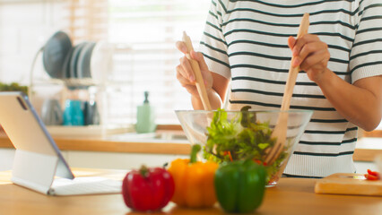 Beautiful young Asian woman hands happy preparing cooking healthy dinner enjoy mix vegetable, green oak lettuce, red bell pepper, tomato, carrot in salad bowl in the cozy kitchen at home