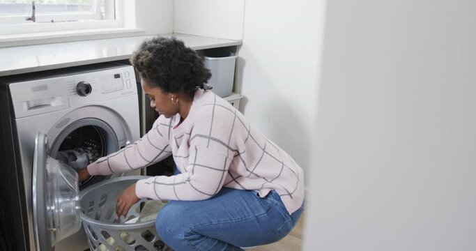 African american woman putting clothes into washing machine, doing laundry at home, slow motion