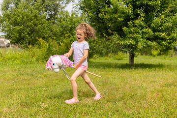 beautiful little girl cowboy playing running riding on toy stick horse in park in nature on summer....
