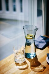 Glass jug on a table filled with a cool, refreshing beverage, with a lemon slice.