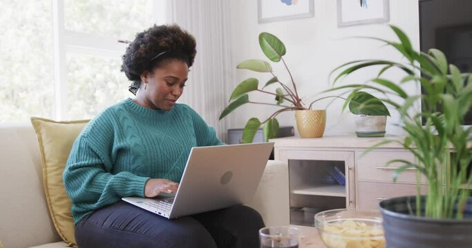 Portrait of happy african american woman sitting on couch using laptop at home, slow motion