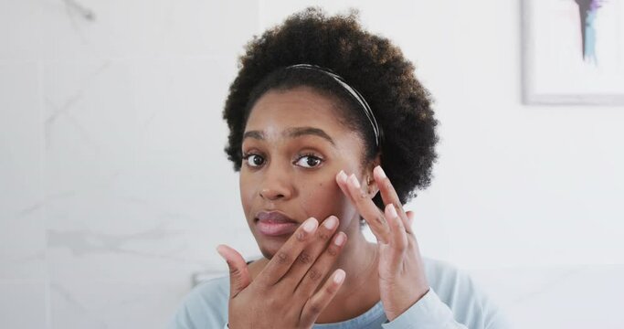African american woman checking her skin, looking at face in bathroom mirror, slow motion