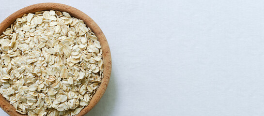 Raw oatmeal in a wooden bowl on a white background. Concept of healthy eating. Vegetarian and vegan food. Rustic style. Horizontal orientation. Selective focus. Copy space. Banner