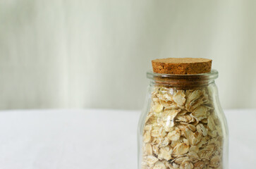 Raw oatmeal in a glass jar with a cork lid on a white background. Concept of healthy eating. Vegetarian and vegan food. Rustic style. Horizontal orientation. Selective focus. Copy space.