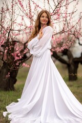 Obraz na płótnie Canvas Woman peach blossom. Happy curly woman in white dress walking in the garden of blossoming peach trees in spring