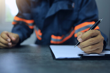 An industrial or shipping inspector auditor supervisor in a reflective jacket is writing a pen on a...