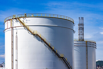 White oil storage fuel tanks at depot station with access ladder against a blue sky. Vertical fuel...