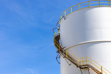White oil storage fuel tanks at depot station with access ladder against a blue sky. Vertical fuel tank staircase.Oil and gas industry.curve line spiral staircase on storage fuel tank.Oil industry,