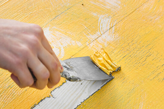 Removing yellow paint with a spatula. Cleaning a wooden surface from paint.