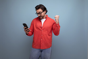 joyful caucasian brunette 30s man in a red shirt looks into the phone