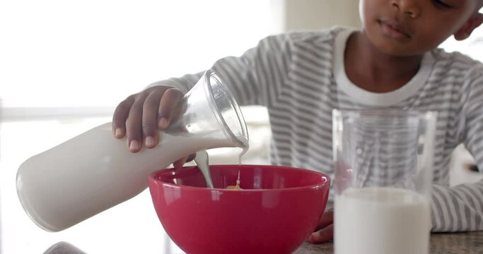African american boy having breakfast pouring milk on cereal in kitchen, slow motion